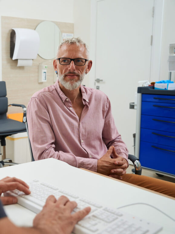 Bearded male with glasses at a doctors appointment, the men are seated at the office desk